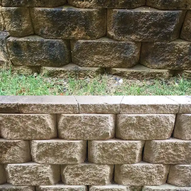 Block retaining wall half cleaned, black mold on top and washed stone below