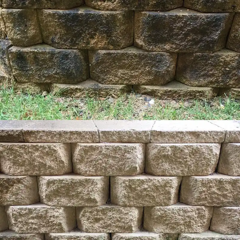 A segmental block retaining wall: the upper rows streaked black with mold, the lower rows washed clean to warm gray
